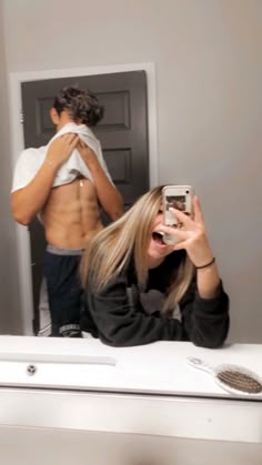 a woman taking a selfie in front of a mirror with her shirt off and the man behind her