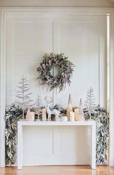 a white table topped with candles and wreaths next to a wall mounted christmas tree