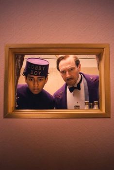 two men in tuxedos are looking at the camera through a mirror that is hanging on a wall