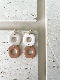 two pairs of white and brown earrings hanging from hooks on a marble wall next to a window