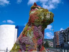 a large dog made out of flowers in front of a building with a sky background