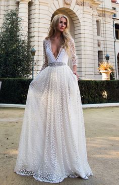 a woman standing in front of a large building wearing a white dress with polka dots on it