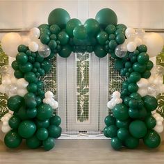 a bunch of balloons that are in front of a wall with a green and white balloon arch