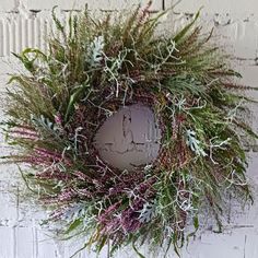 a wreath hanging on the side of a white brick wall with purple flowers and greenery