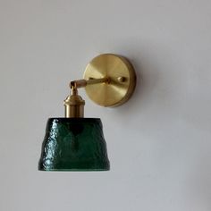 a green glass light hanging from the side of a wall mounted lamp on a white wall