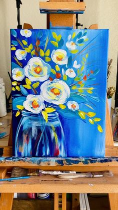 an easel with paint and flowers on it in front of a blue painting board