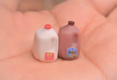 two small plastic milk bottles sitting on top of each other in someone's hand