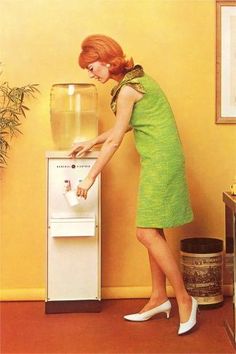 a woman standing next to an old fashioned water dispenser in a yellow room