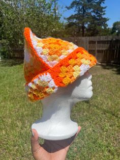 a white mannequin head wearing an orange and yellow crocheted hat