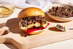 a sandwich with meat and vegetables on a cutting board next to a bowl of salad