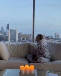 a woman sitting on top of a couch next to a table with candles in front of her