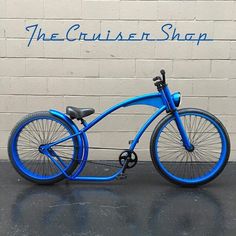 a blue bicycle parked in front of a white brick wall with the cruiser shop written on it