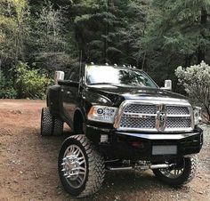 a black ram truck parked on top of a dirt road in front of some trees