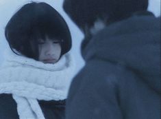 two people standing outside in the snow with one person wearing a white scarf and black coat