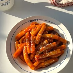 a white plate topped with carrots covered in sauce next to a cup of coffee