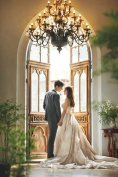 a bride and groom standing in front of an arched doorway with chandelier above them