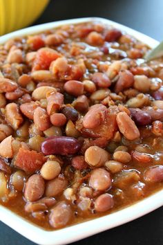 a white bowl filled with beans and meat on top of a black table next to a banana