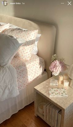 a bed with white sheets and pink flowers on top of it next to a night stand