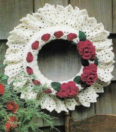 a crocheted wreath with red flowers on it next to a wooden chair and pot holder