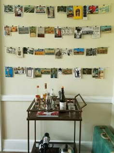 a bar cart in front of a wall with pictures on it and wine bottles next to it