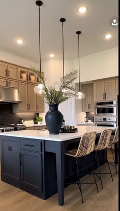 a large kitchen with an island in the middle and chairs at the end, along with lights hanging from the ceiling