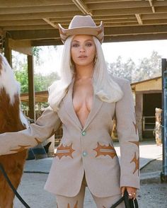 a woman in a cowboy hat standing next to a brown and white horse wearing a suit