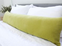 a large green pillow sitting on top of a bed next to pillows and a plant