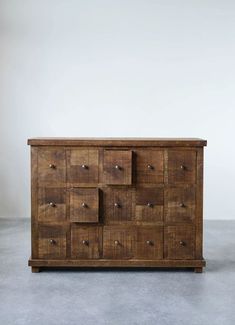 an old wooden dresser with many drawers and knobs on the top, in front of a white wall