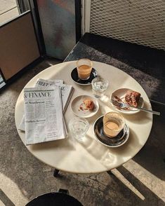 a table topped with plates and cups filled with food next to a newspaper on top of a table