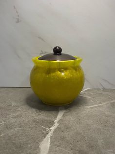 a yellow pot with a black lid sitting on a marble floor next to a white wall