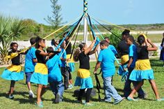 a group of people in blue and yellow dresses holding up a large kite on top of grass