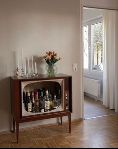 an old fashioned television set with liquor bottles on the cabinet and candles in front of it