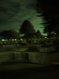 a blurry photo of a cemetery at night with trees in the foreground and dark clouds in the background