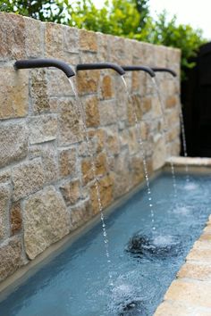 a stone wall with water running from it and two faucets in the middle