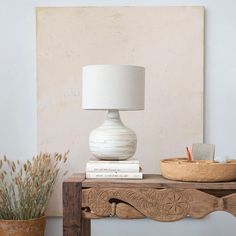 a white lamp sitting on top of a wooden table next to a potted plant