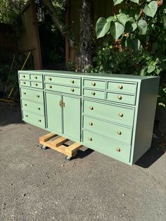 a green dresser sitting on top of a wooden pallet in front of a tree