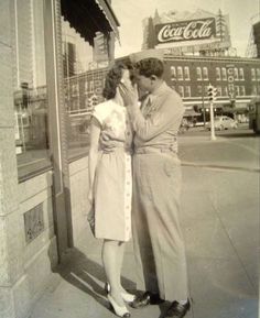 an old black and white photo of two people kissing in front of a coca cola sign