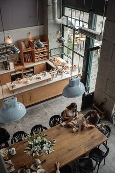 a woman sitting at a wooden table in front of a counter filled with pastries