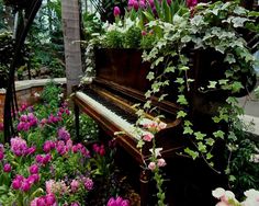 an old piano is surrounded by flowers and greenery