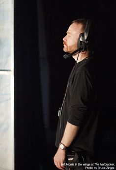 a man with headphones on standing in front of a black wall and looking off to the side