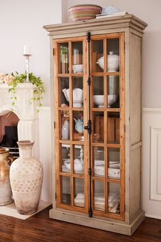 a wooden cabinet with glass doors in a living room next to a vase and potted plant