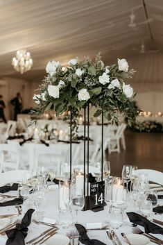 an elegant centerpiece with white flowers and greenery sits atop a black - and - white table cloth