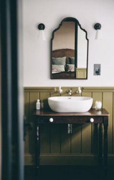 a bathroom sink sitting under a mirror next to a wooden table with candles on it