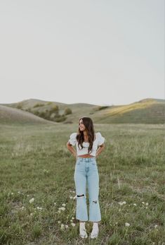 a woman standing in the middle of a field with her hands on her hips and looking up