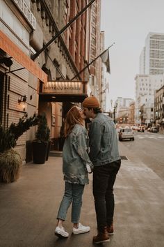 a man and woman are standing on the sidewalk in front of a building, facing each other