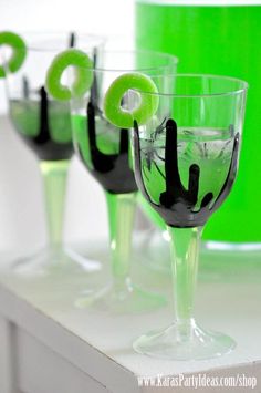 three glasses with black and green liquid in them sitting on a white table next to a lime