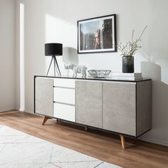 a white and black sideboard sitting on top of a wooden floor next to a lamp