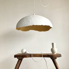 a wooden table topped with two white vases and a light hanging from the ceiling