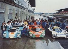 a group of men standing next to two race cars