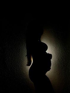 the silhouette of a pregnant woman against a dark wall